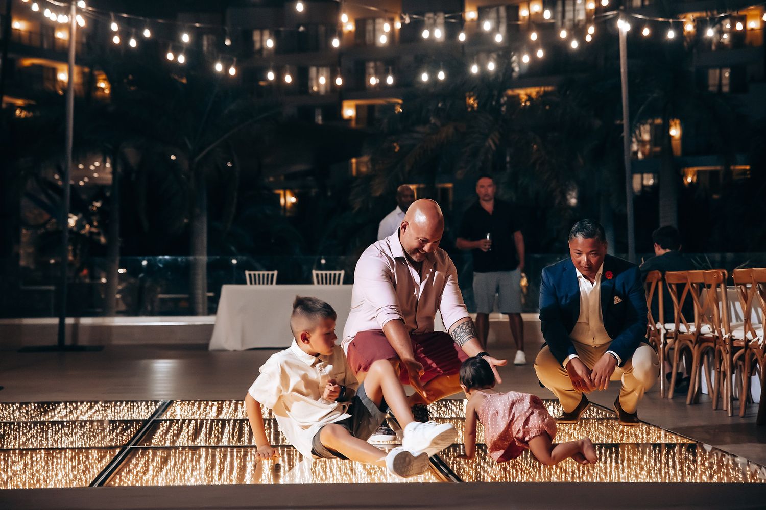 Evening celebration under string lights with people sitting on wooden platform.
