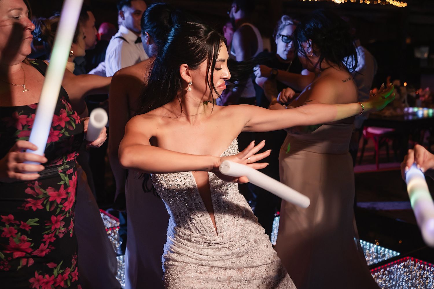 Wedding party dancing and celebrating on a dimly lit dance floor with string lights overhead.