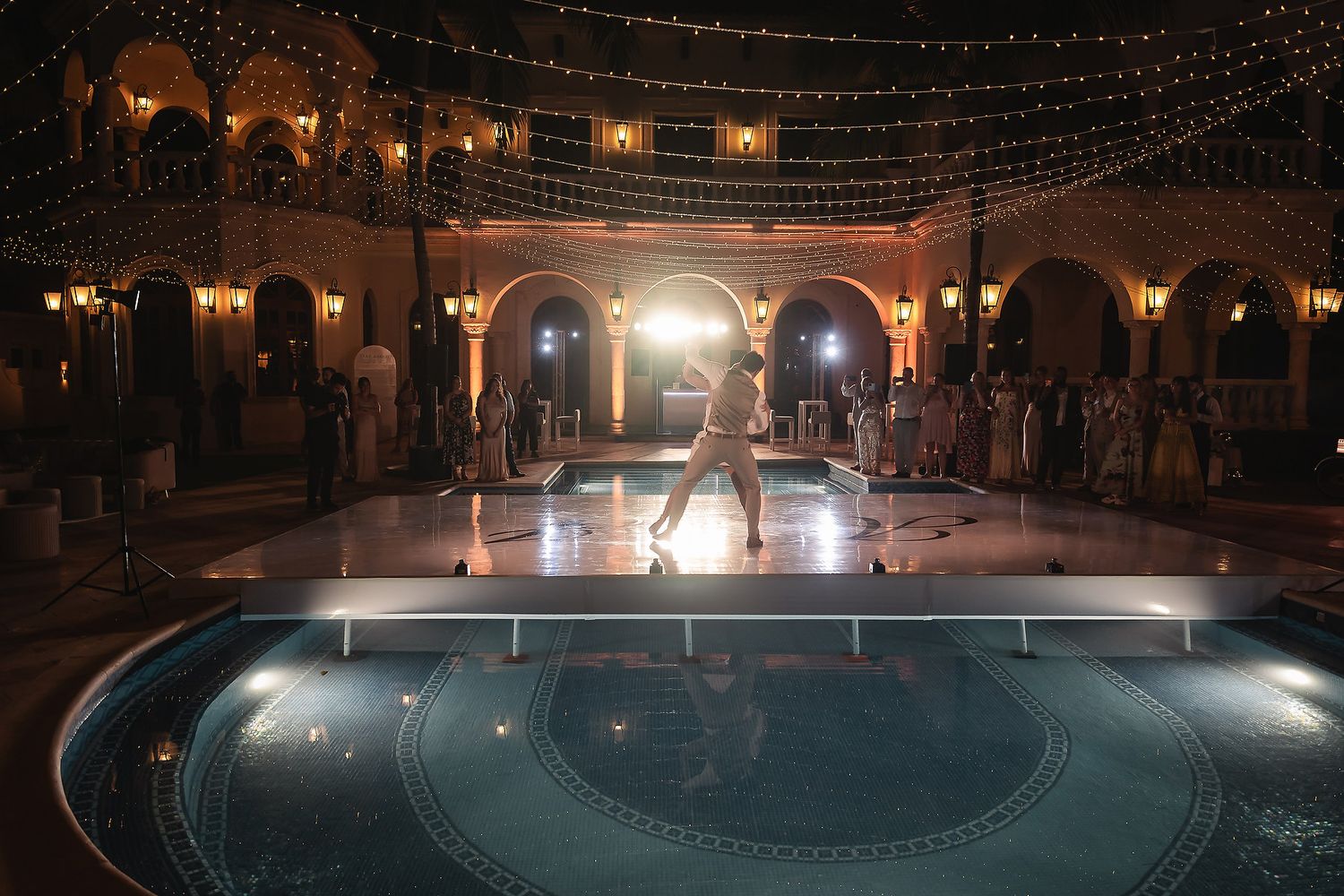 Elegant nighttime dance performance by pool with string lights and arched architecture.