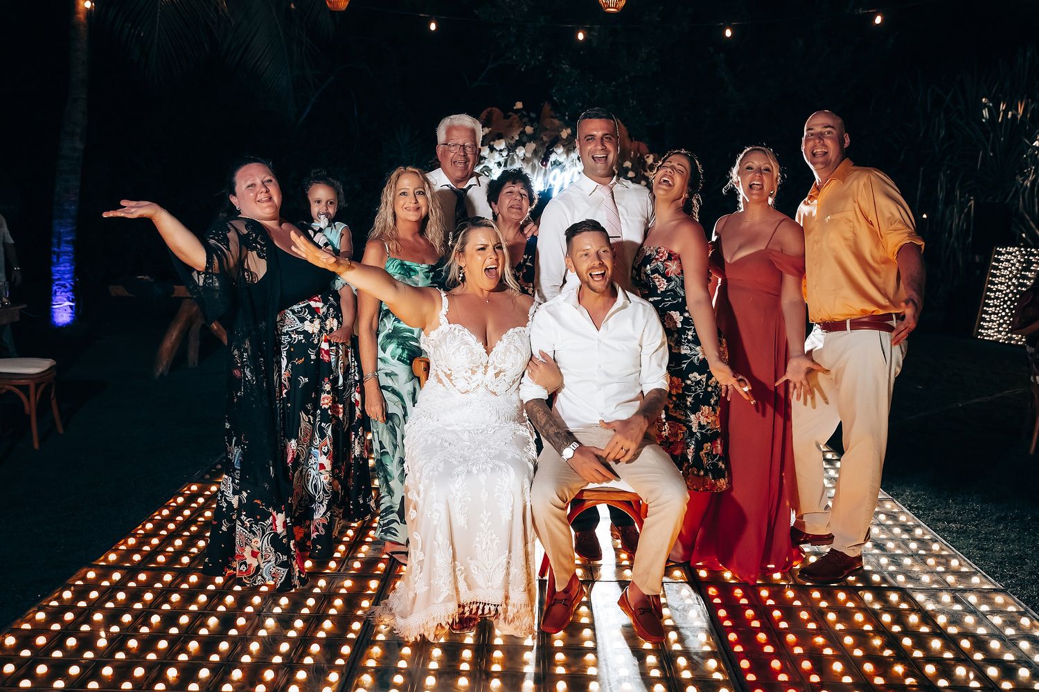 Evening wedding celebration with string lights and guests dancing on illuminated dance floor.