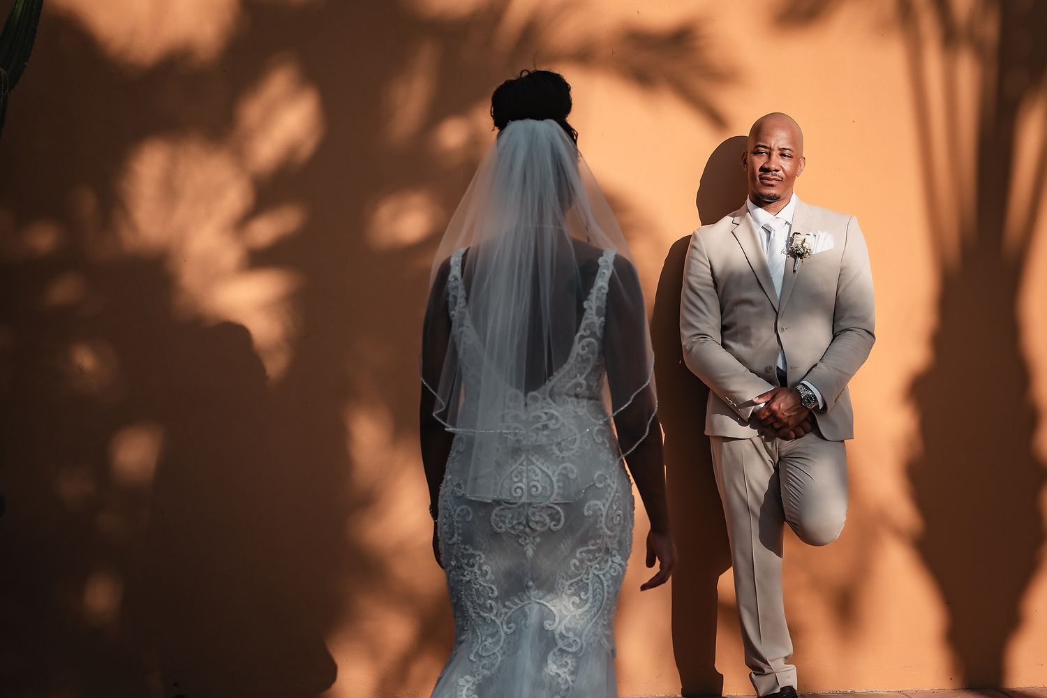 Elegant wedding portraits captured against a warm-toned wall with natural shadows.