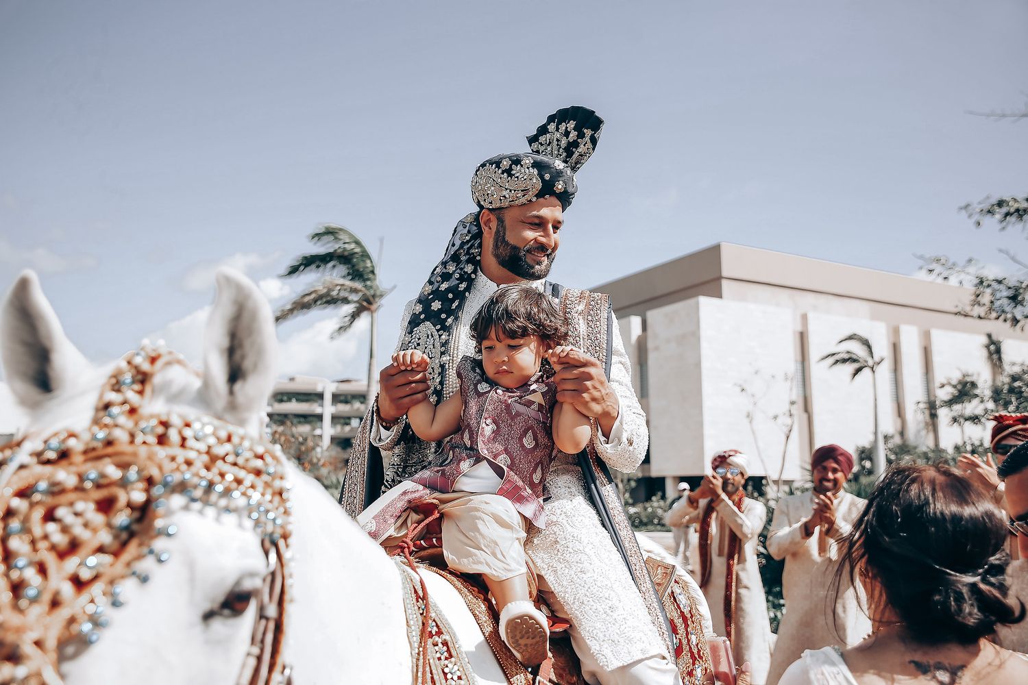 A group of joyful people celebrate outdoors on a sunny day with palm trees in the background.