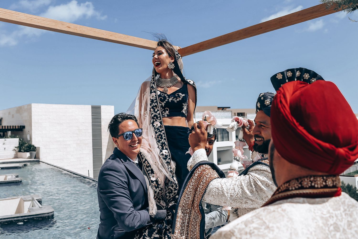 People gather on a boat deck against a bright blue sky and marina backdrop on a sunny day.
