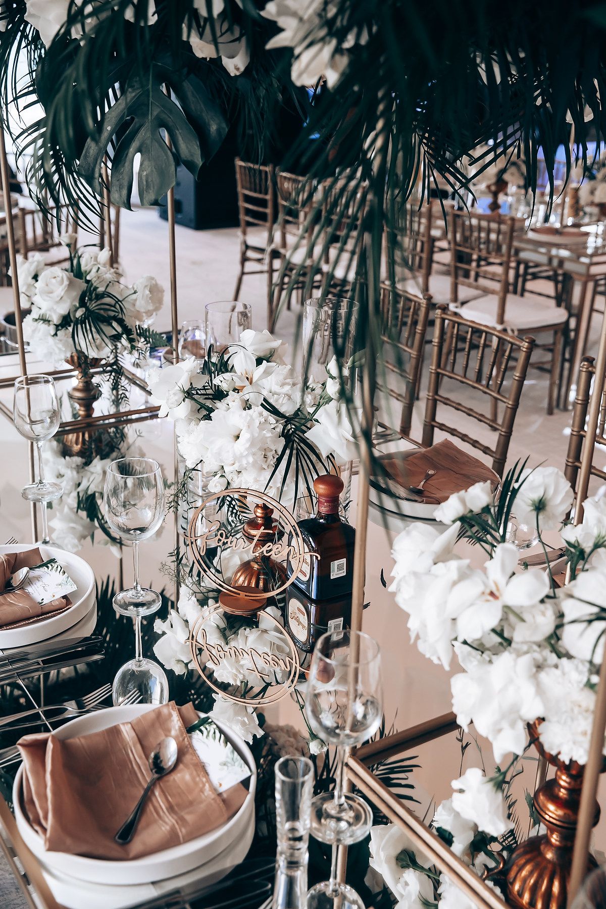 Luxurious wedding reception table setting with hanging orchids and tropical palm leaves.
