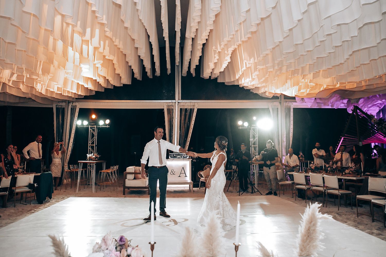 A couple shares their first dance under an elegant white canopy with dramatic lighting at their reception.