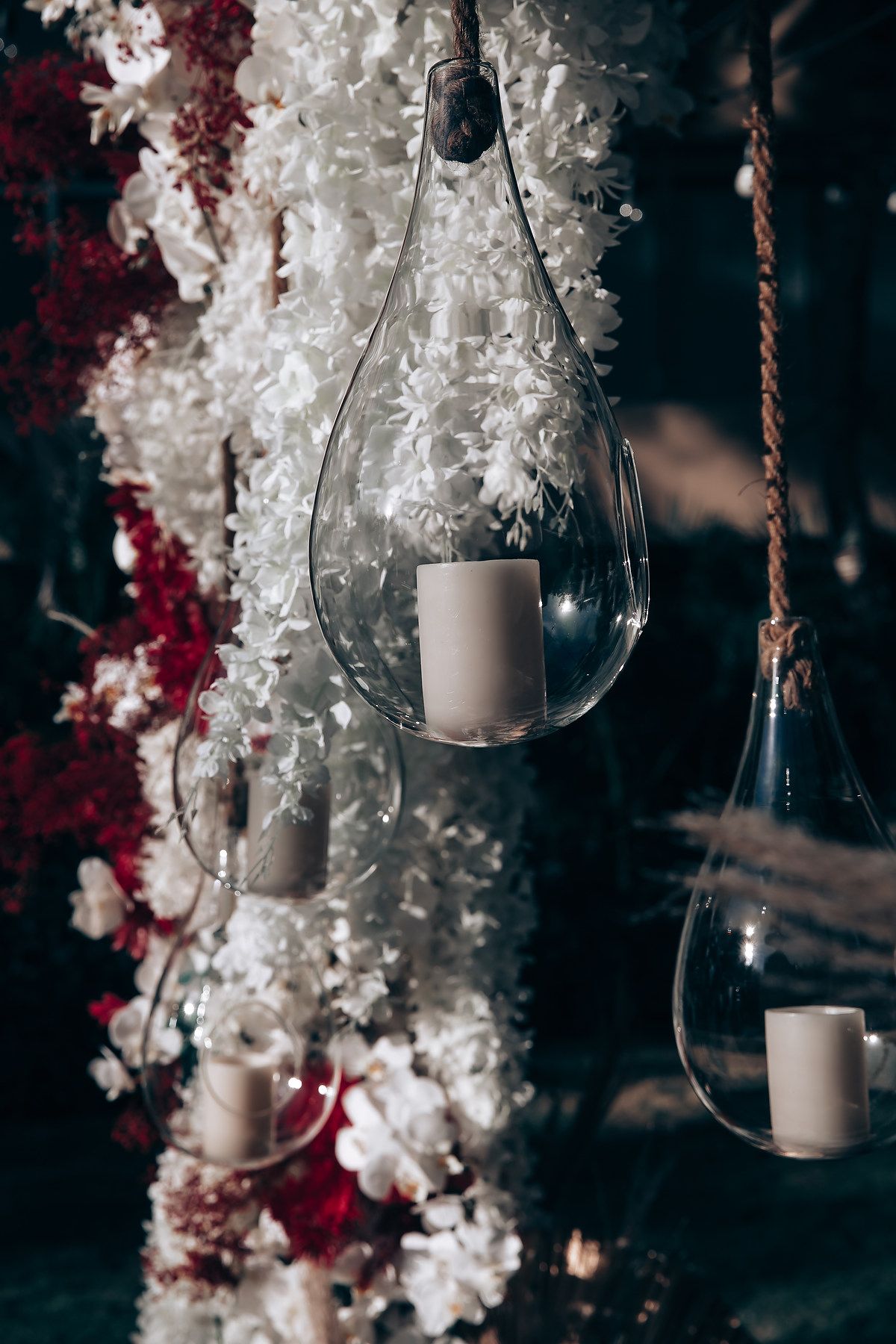 Hanging glass candle holders with white candles surrounded by white and burgundy floral decorations create an elegant ambiance.
