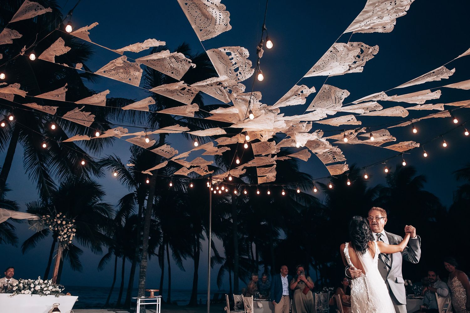 String lights and decorative fabric create a romantic canopy over an evening beach reception.