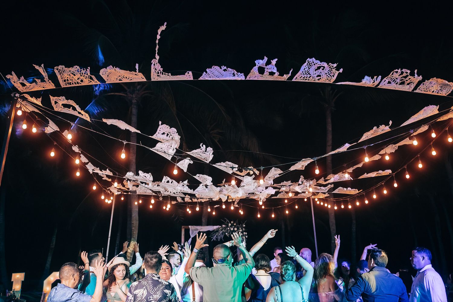 Wedding reception dance floor filled with celebrating guests under twinkling string lights.