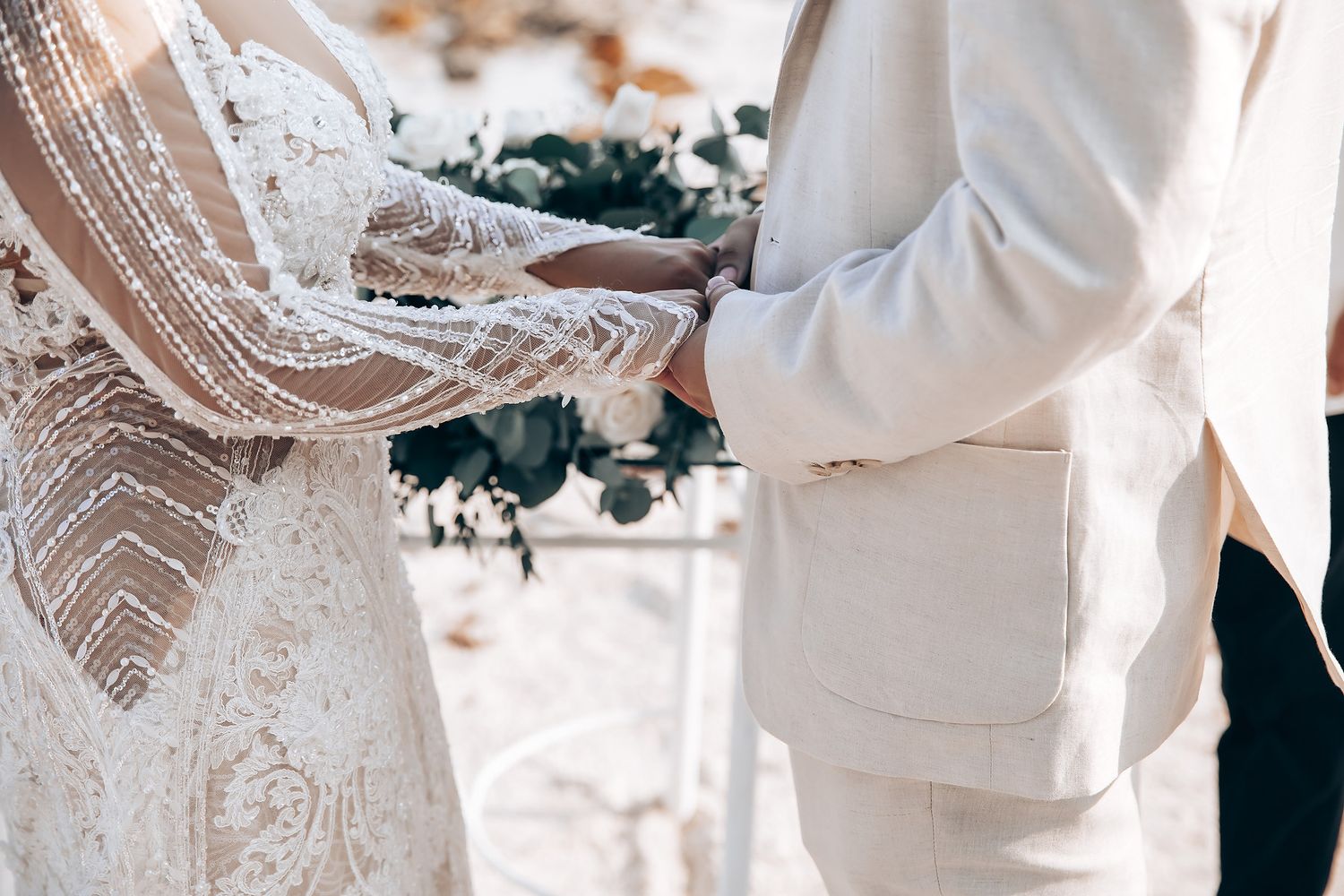 Couple exchanging rings during intimate beach wedding ceremony with white decor and floral arrangements.