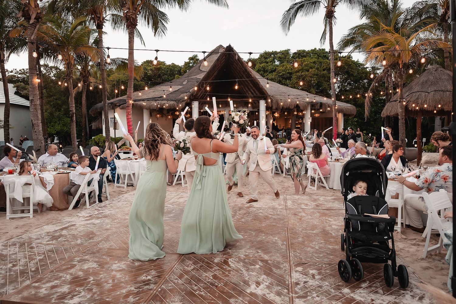 Beach wedding reception setup with white chairs and tropical palm trees at sunset.