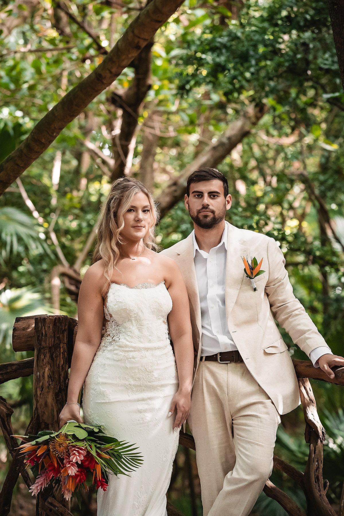 Wedding couple posing among tropical trees and greenery in a garden setting.