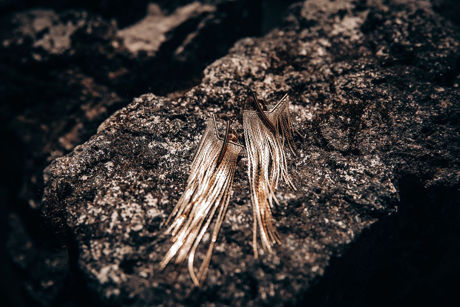 Delicate gold wing-shaped jewelry piece displayed on dark textured stone.