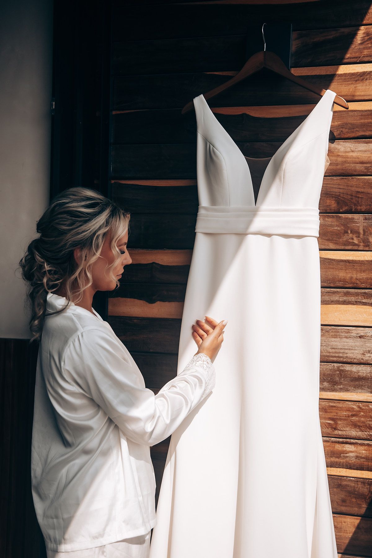 Classic white wedding gown with v-neckline displayed on hanger against wooden wall.