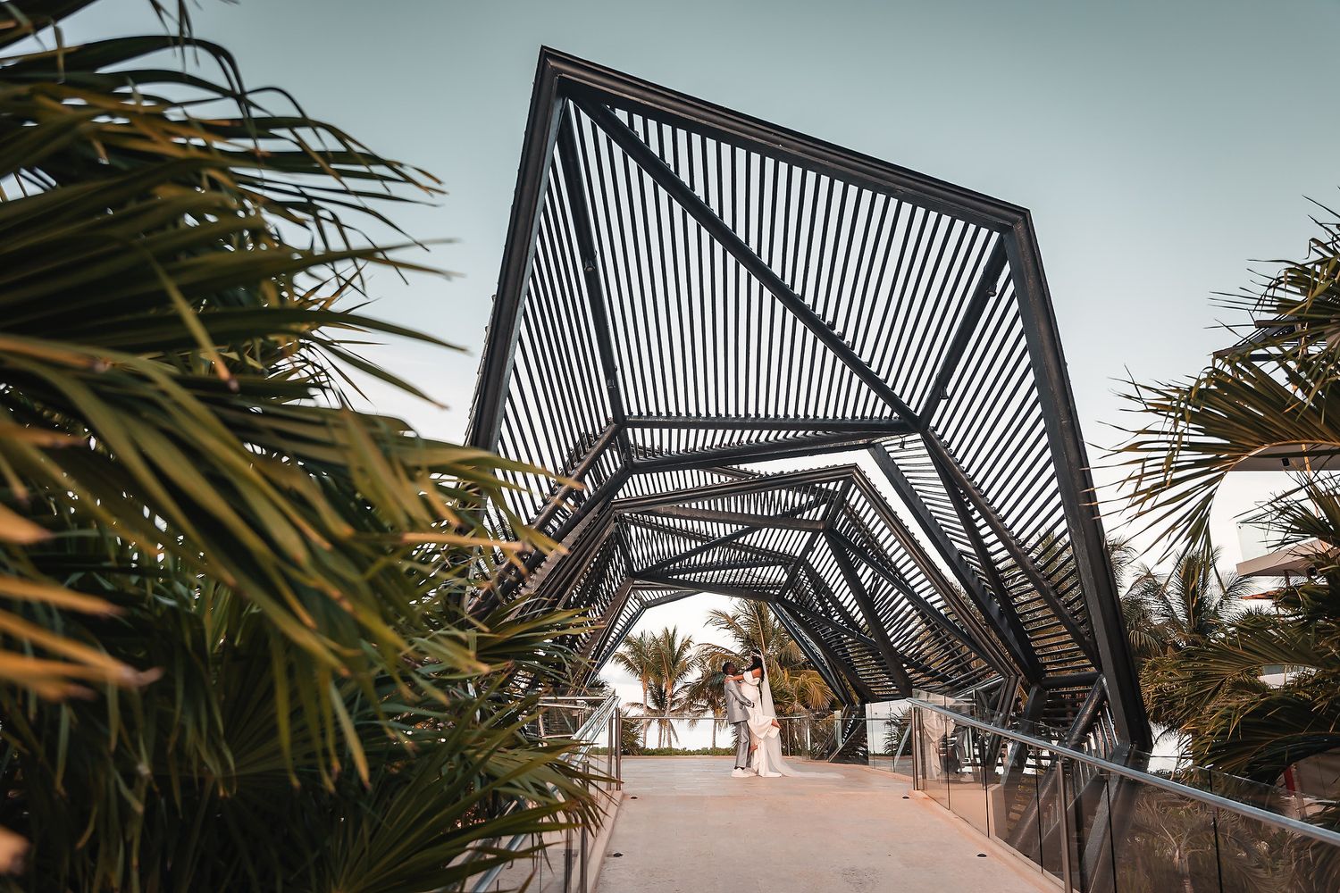 Modern geometric walkway with black metal framework and palm trees at a tropical wedding venue.
