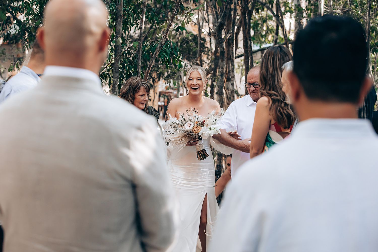 Wedding party gathered outdoors among trees for celebration photos.