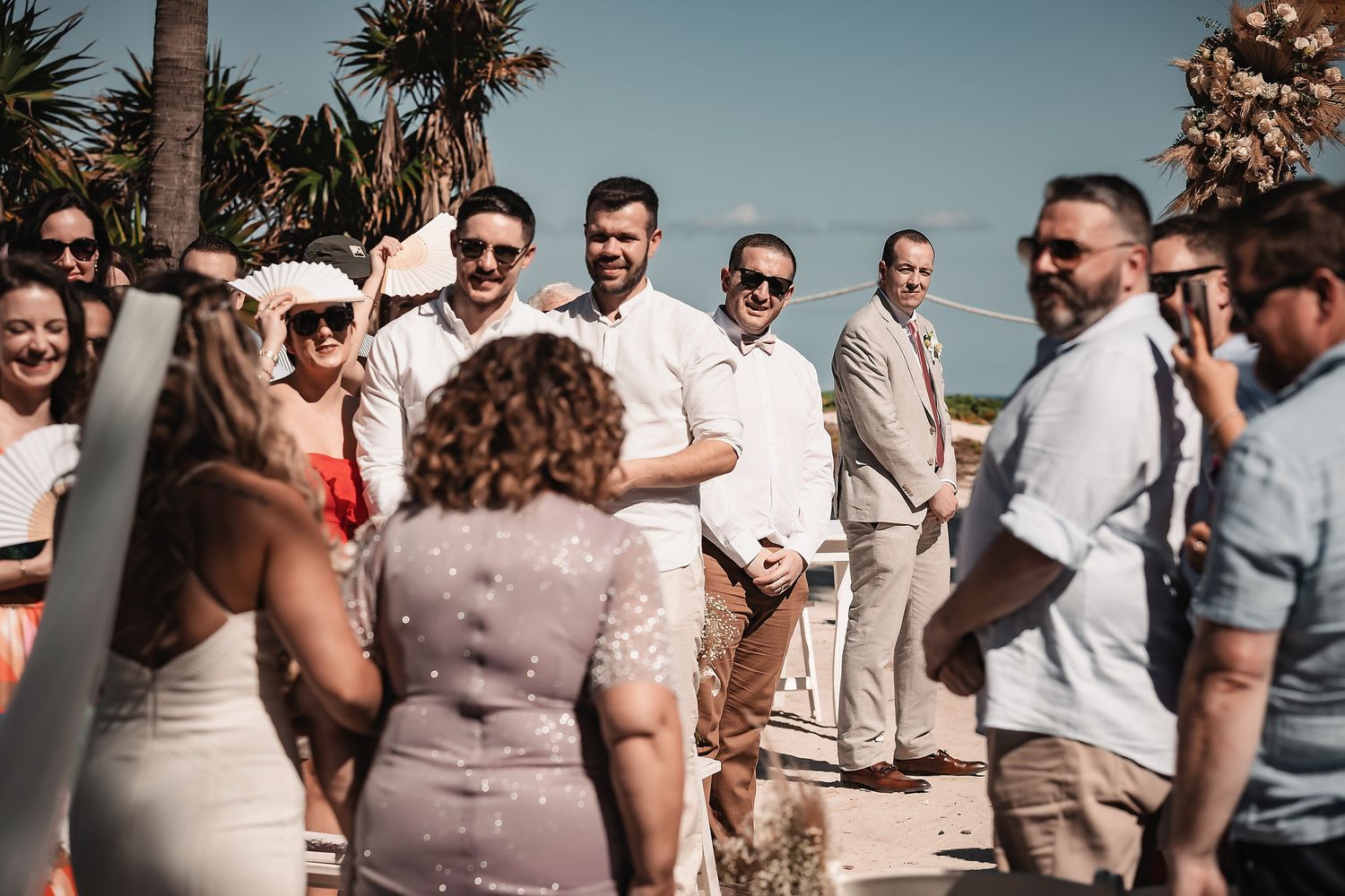Guests smiling and celebrating at an outdoor beach wedding ceremony on a sunny day.