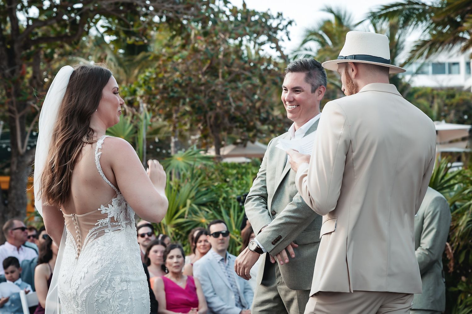 Bride and groom exchange vows at an outdoor beach wedding ceremony with guests seated in the background.