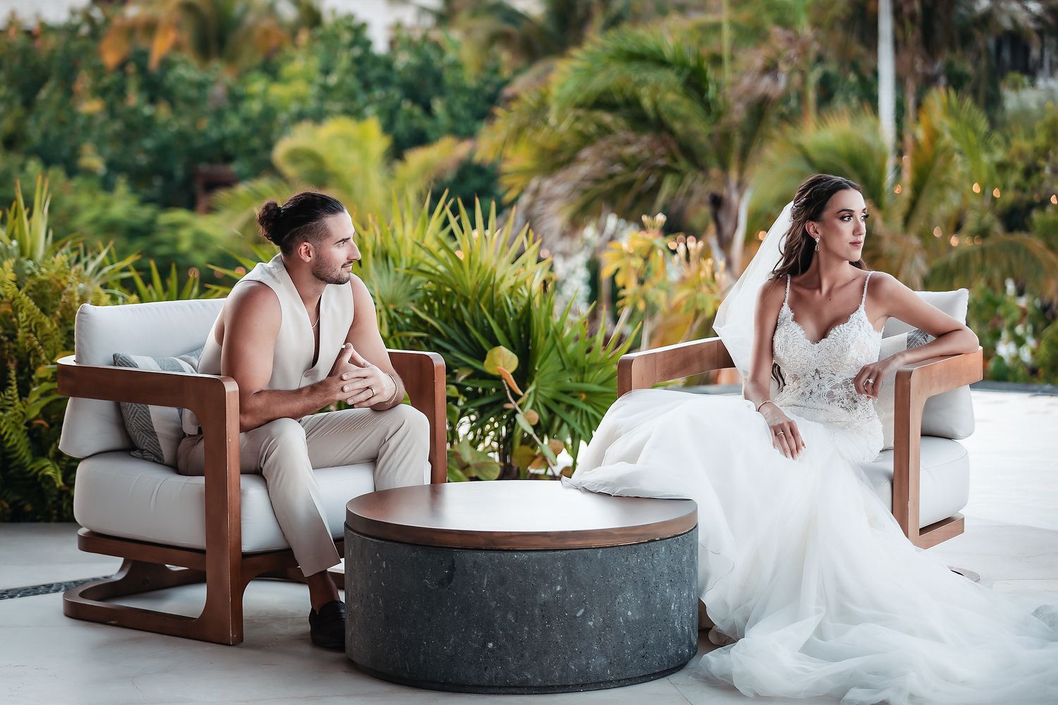 Bride and groom sitting in elegant chairs on a tropical resort terrace during their destination wedding.