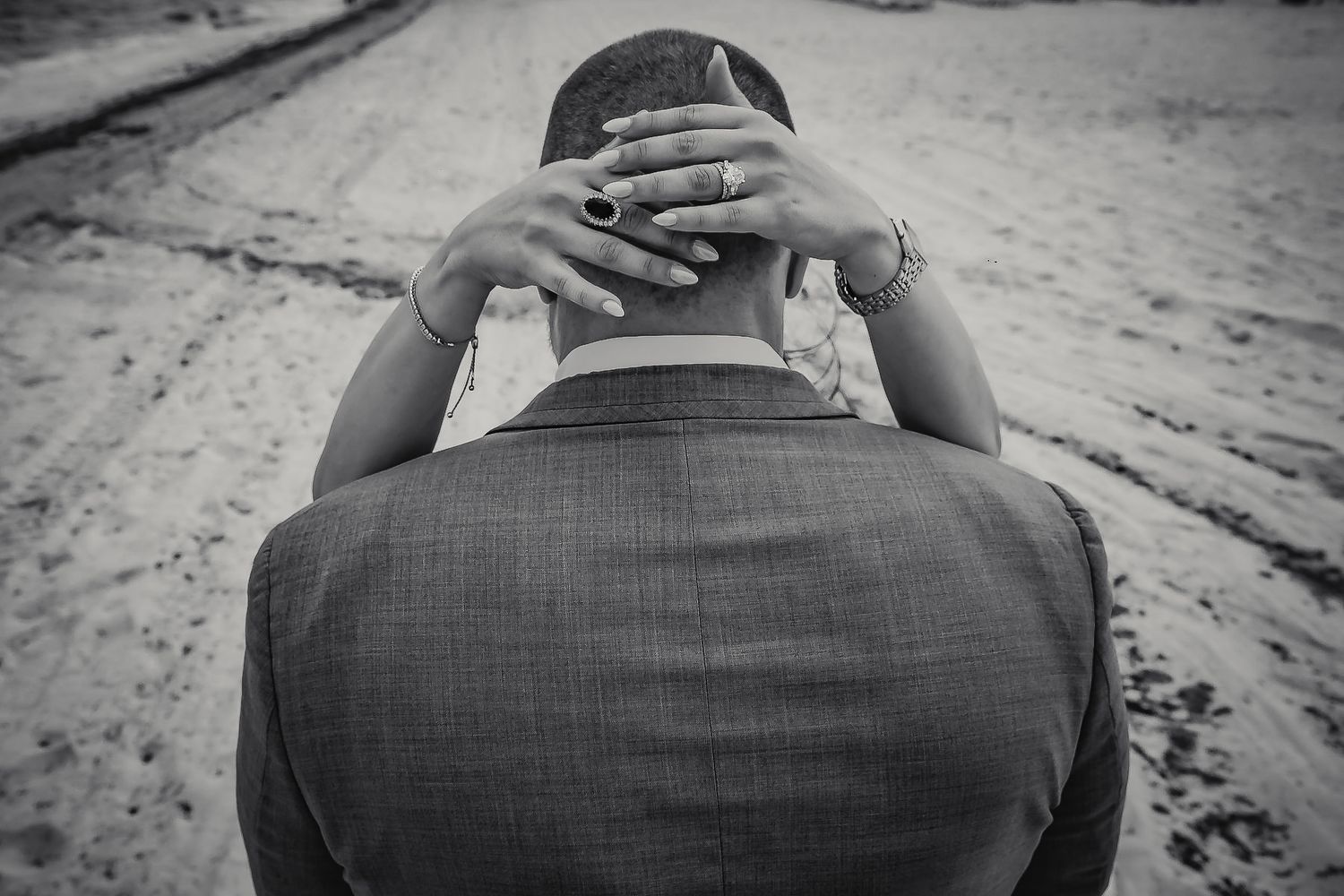 Black and white photo of a couple embracing, bride's hands with ring resting on groom's neck at wedding.