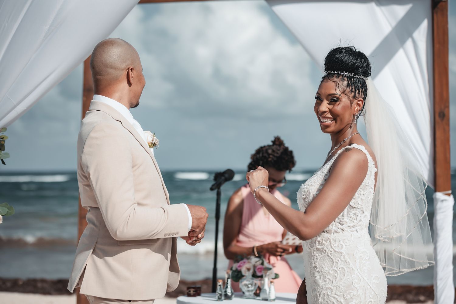 Bride and groom exchange vows at a romantic outdoor beach wedding ceremony, with officiant and ocean in background.