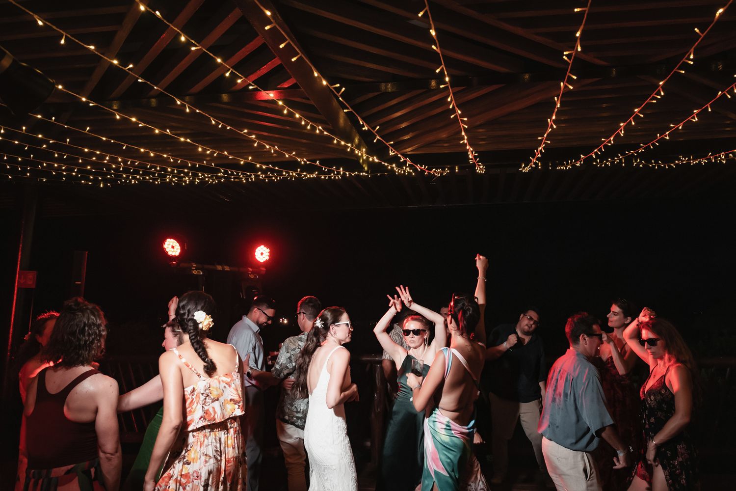 Guests dancing under string lights at a festive outdoor wedding reception at night.