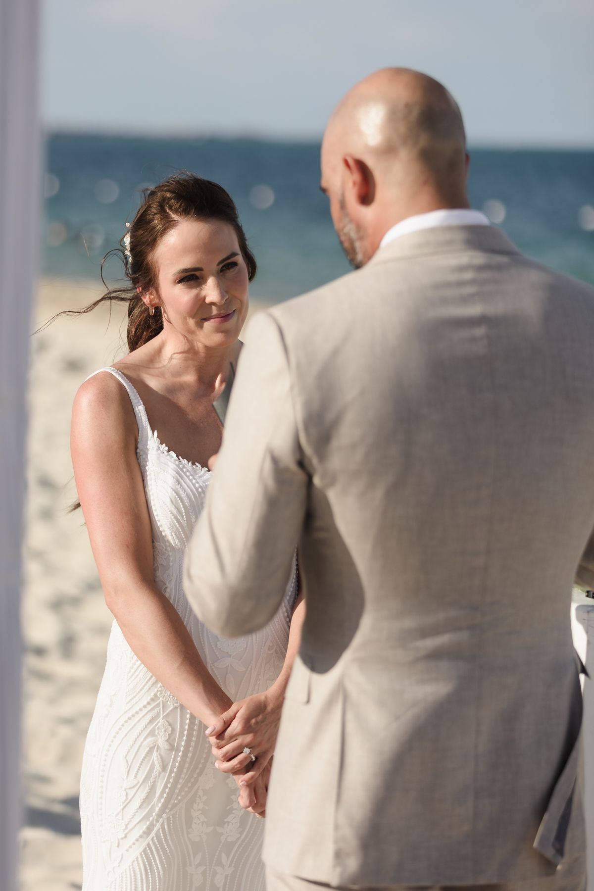 Bride and groom exchange vows during a romantic beach wedding ceremony, with ocean waves visible in the background.
