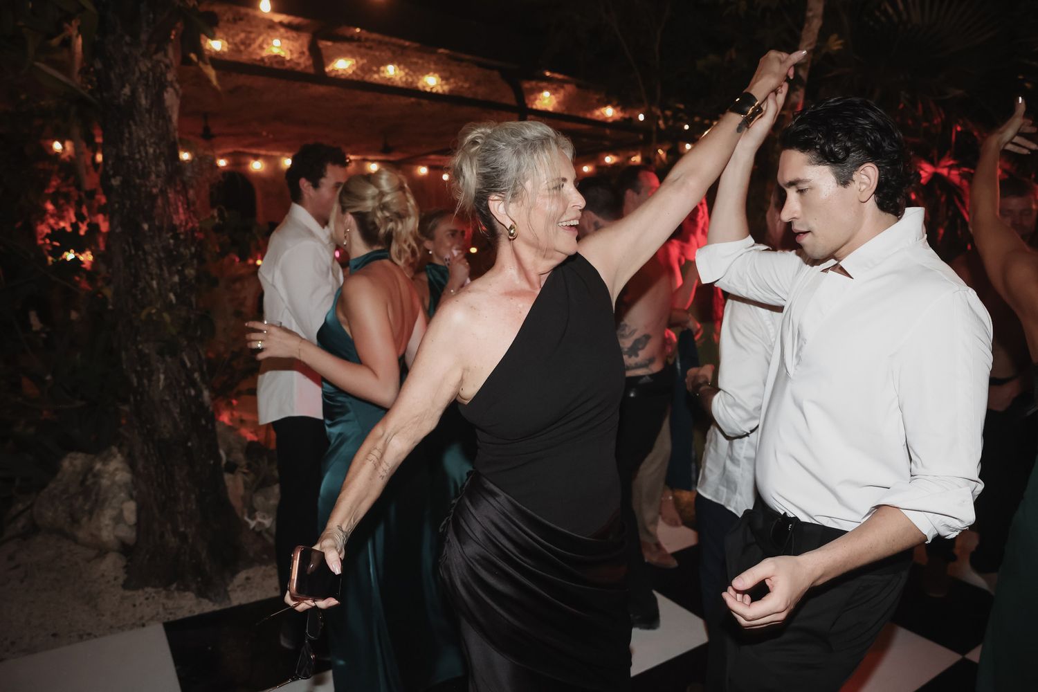 Elderly woman in green dress dancing with young man in white shirt at an elegant outdoor evening party.