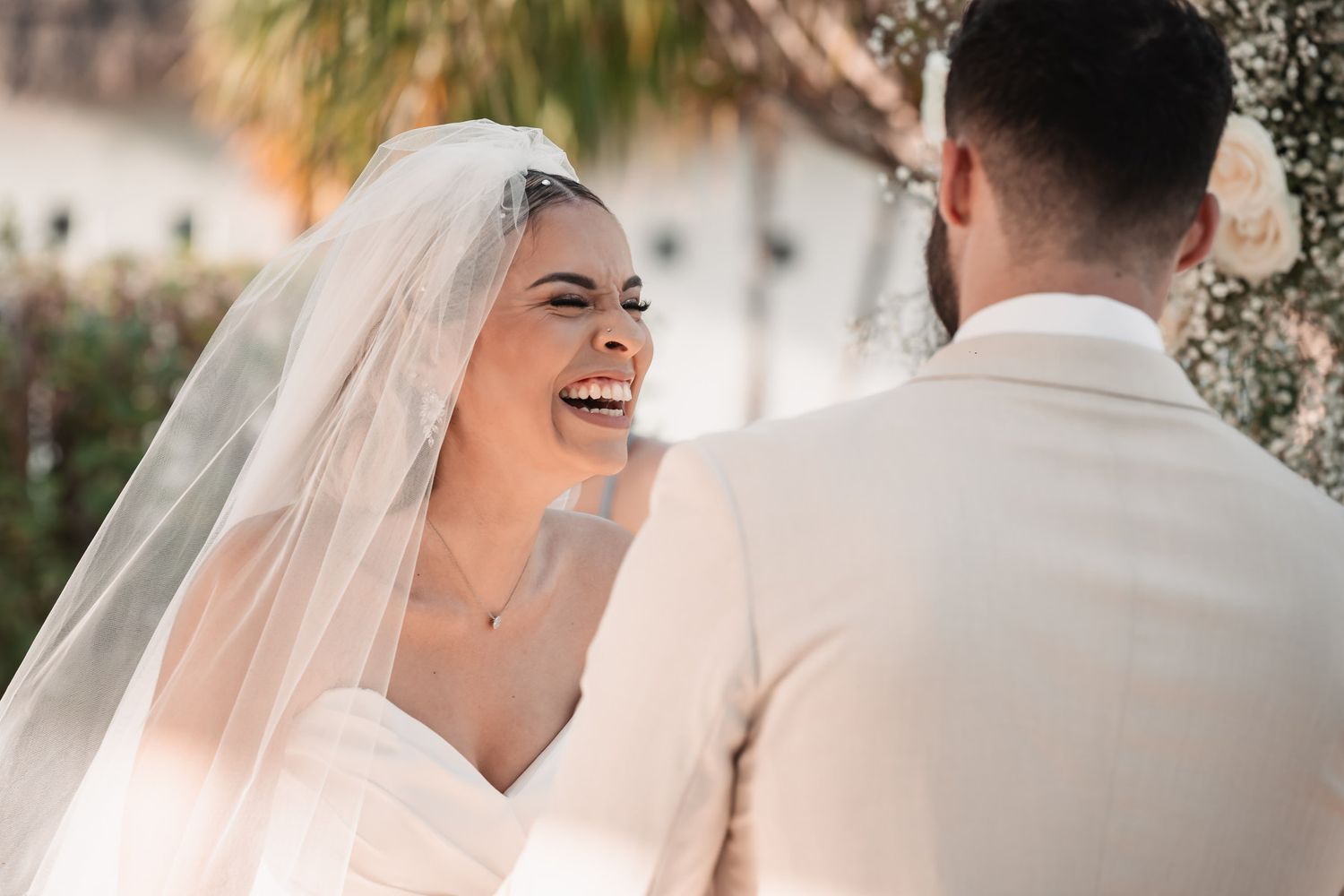 Joyful bride in veil laughing during first look with groom.