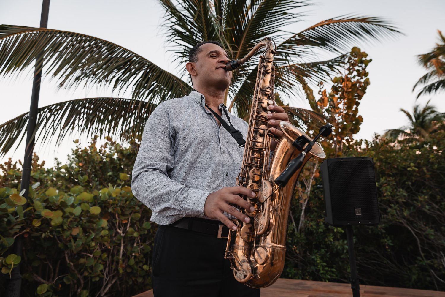 Saxophonist performing outdoors at sunset with tropical palm trees in the background at a wedding.