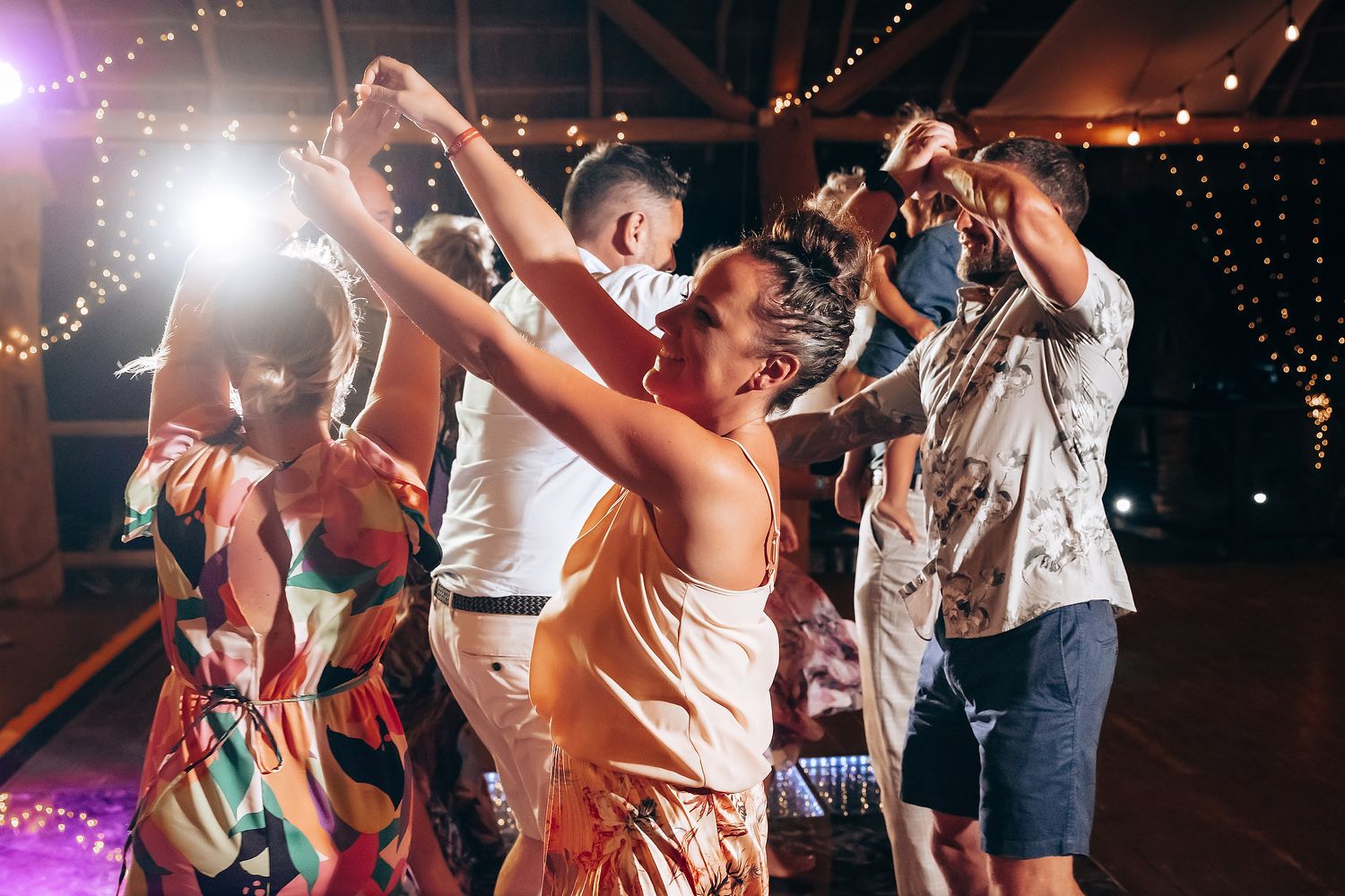 Energetic dancers enjoying themselves at a nighttime party with twinkling lights in the background.
