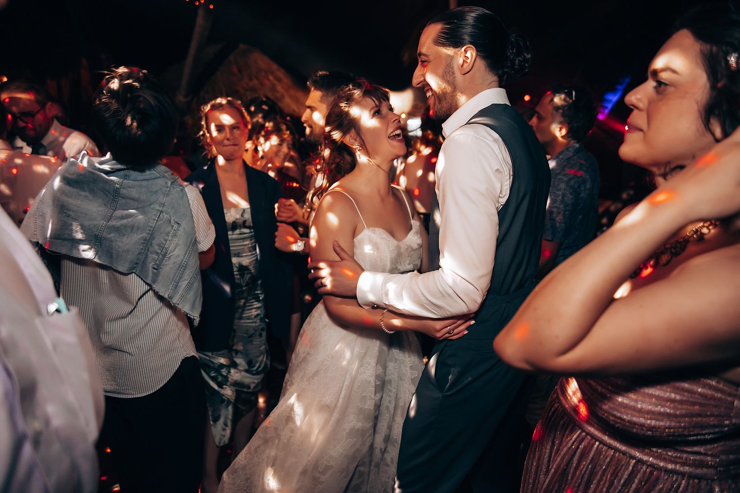 Wedding guests dancing and celebrating at dimly lit reception party.