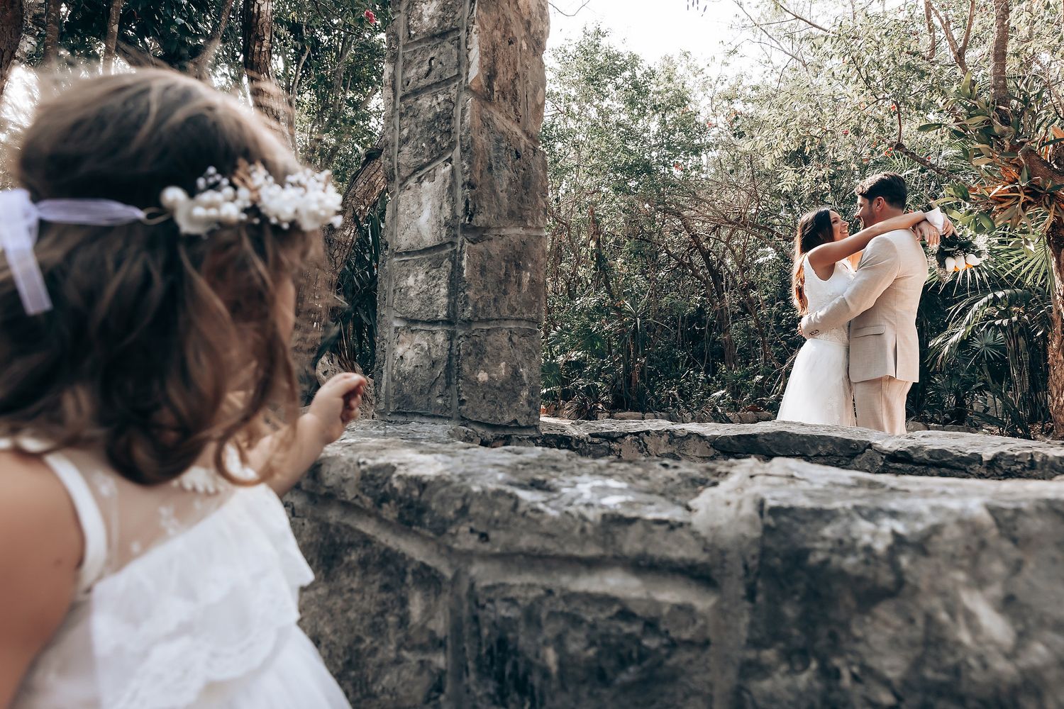 A dreamy outdoor wedding scene with stone walls and natural greenery in the background.