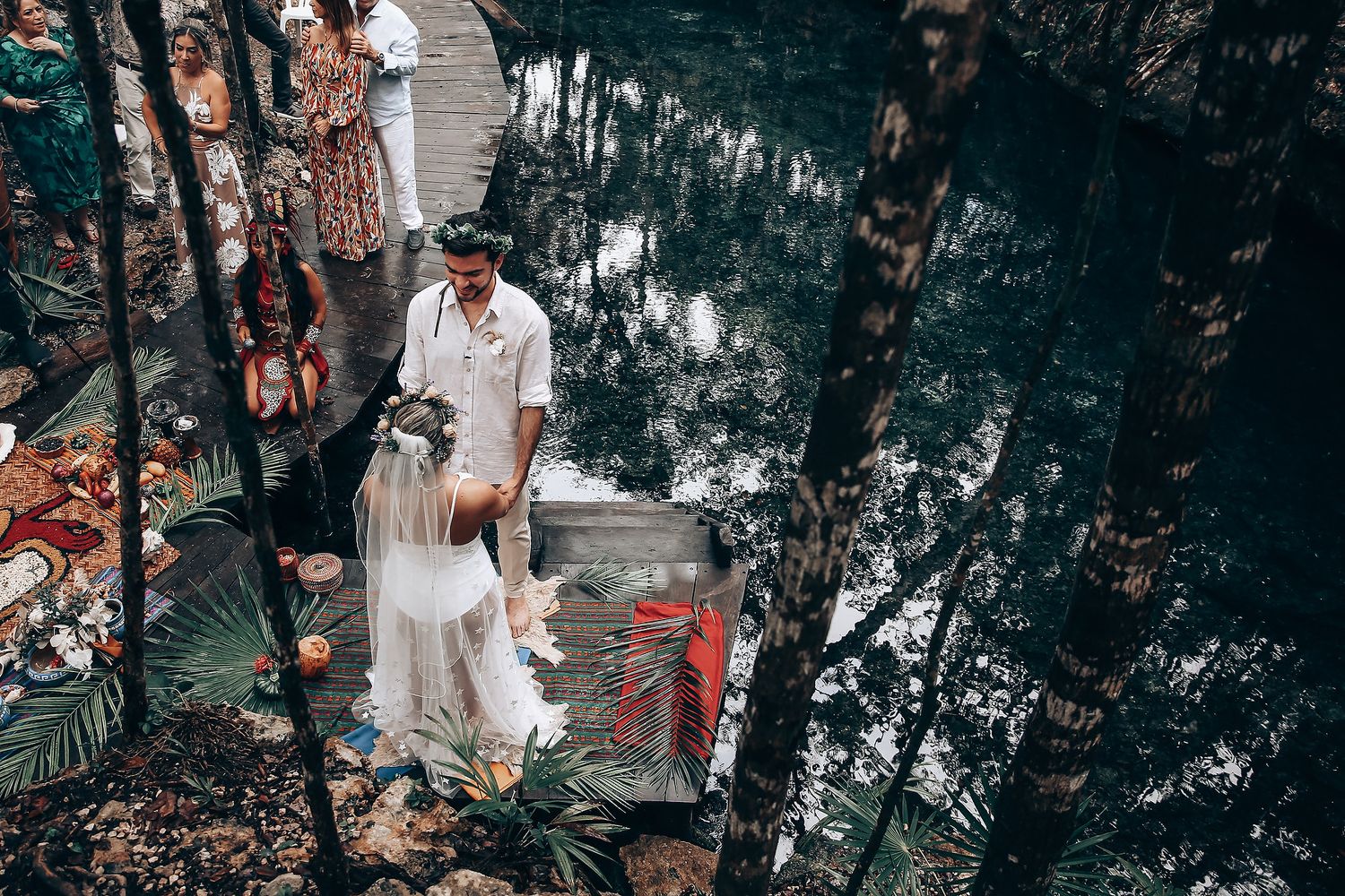 A couple descends stone steps in a lush forest setting during what appears to be a wedding ceremony.