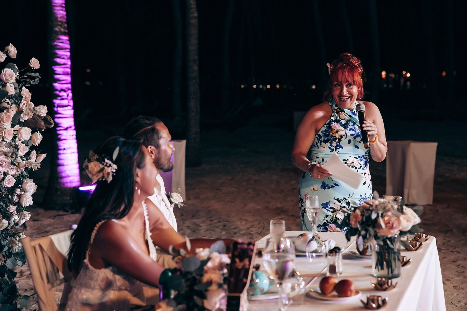 Evening wedding reception with purple ambient lighting and floral decorations.