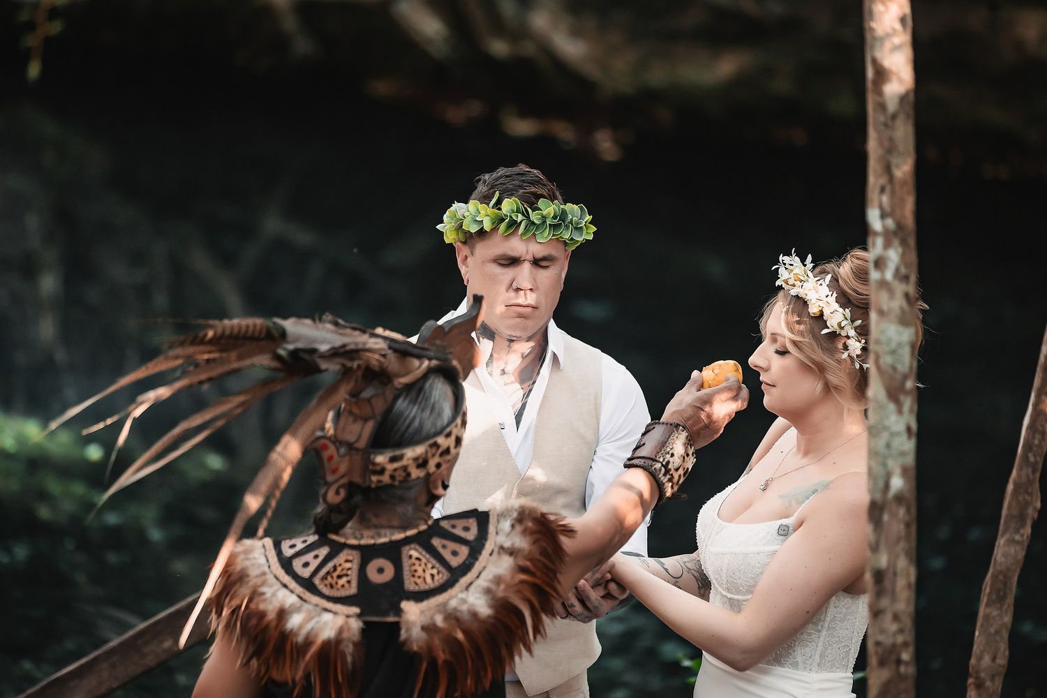 Bride and groom participating in a Mayan ritual ceremony outdoors, surrounded by lush jungle scenery.