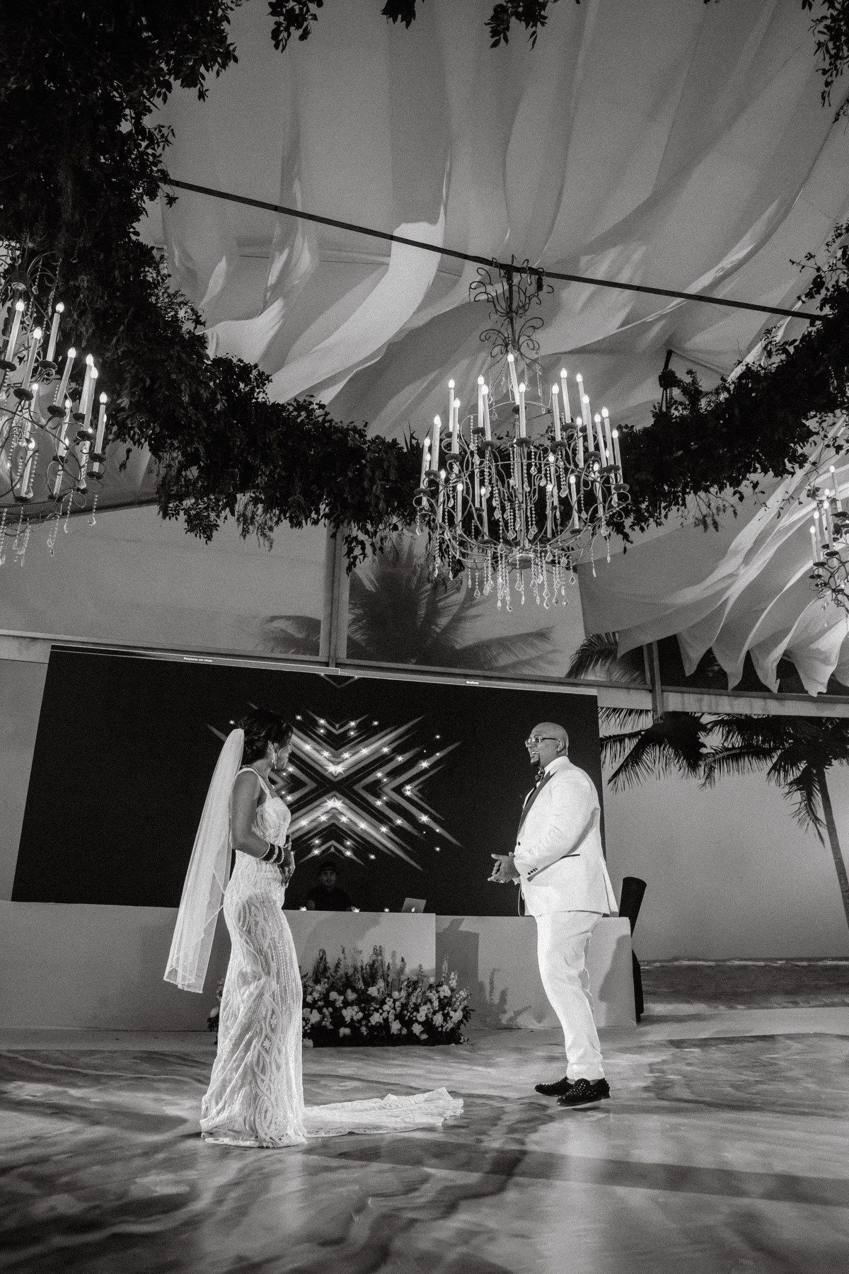 Black and white photo of bride and groom sharing first dance under chandeliers.