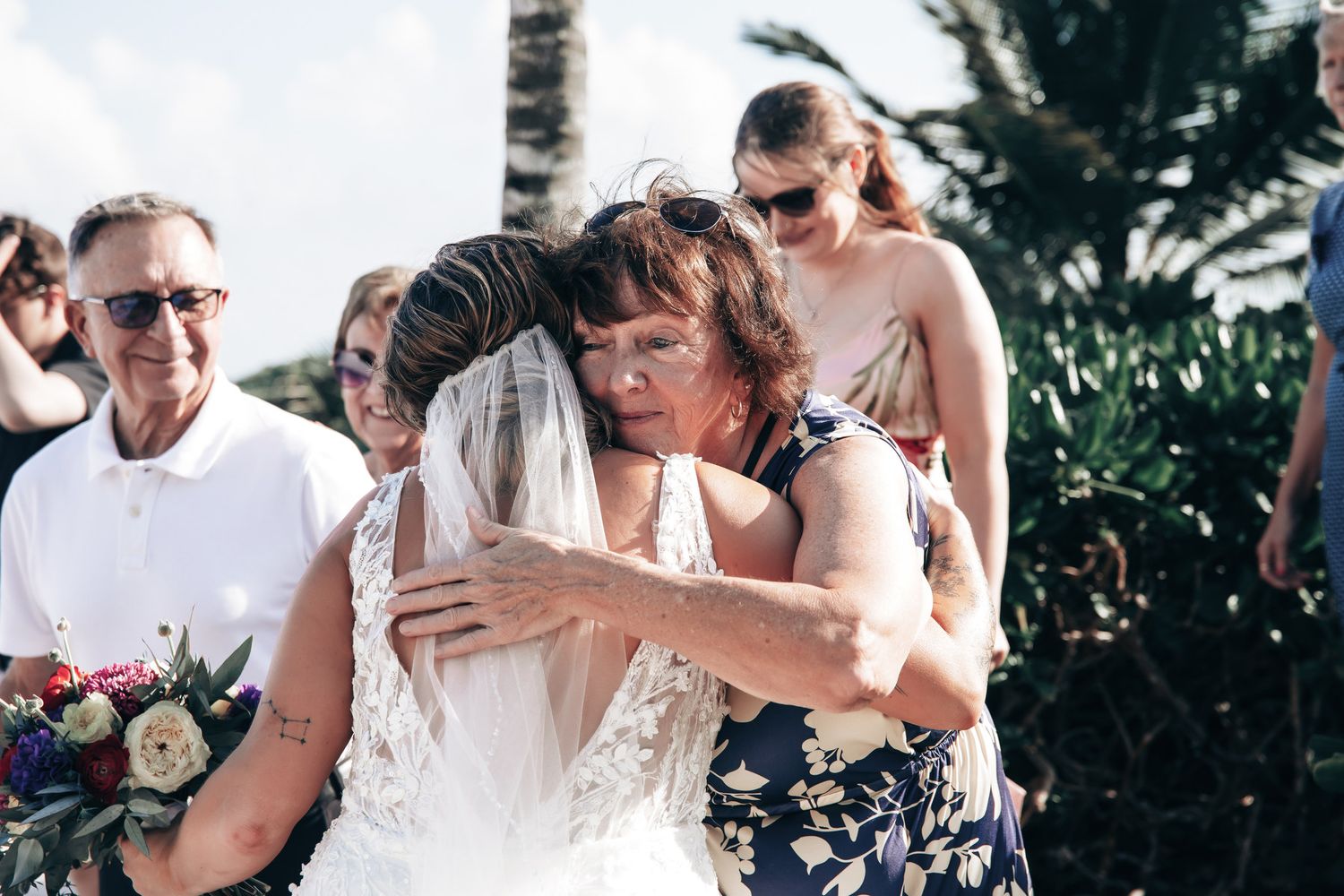 Emotional wedding moment as bride receives a warm embrace from a loved one holding a bridal bouquet.