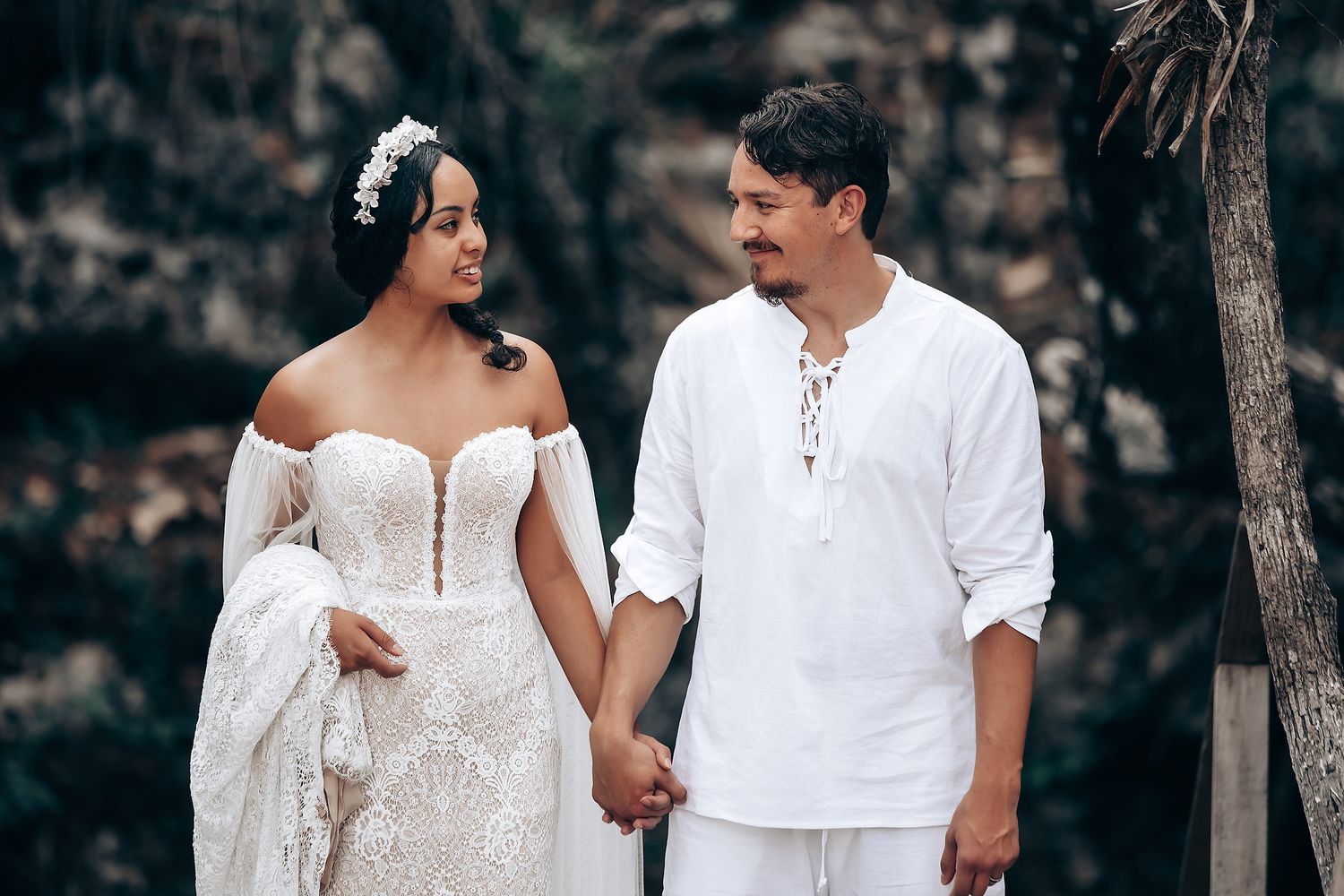 A romantic outdoor photoshoot with a couple in white outfits walking together in a natural setting.