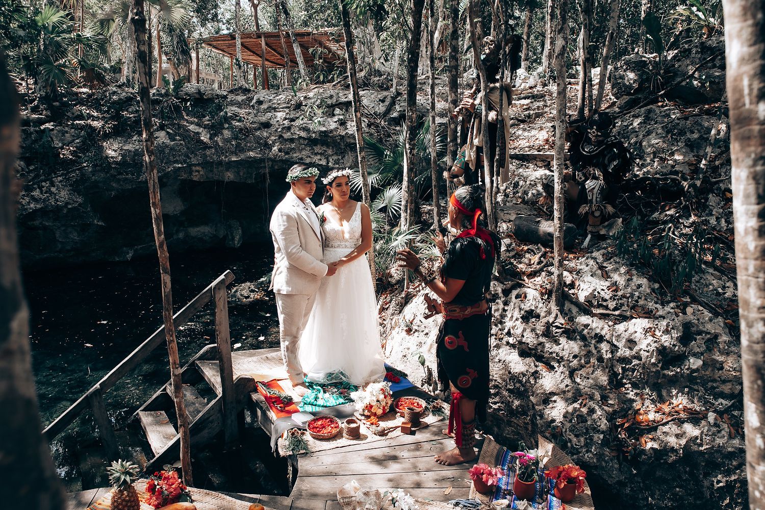 Wedding ceremony taking place in a natural cave setting with rock formations and forest backdrop.