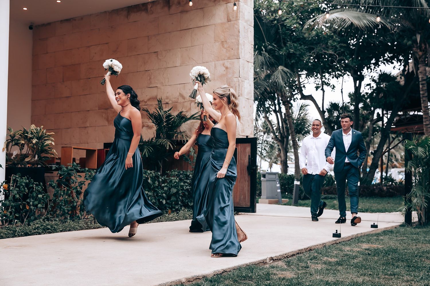 Wedding party members sliding down a grassy hill in playful poses.