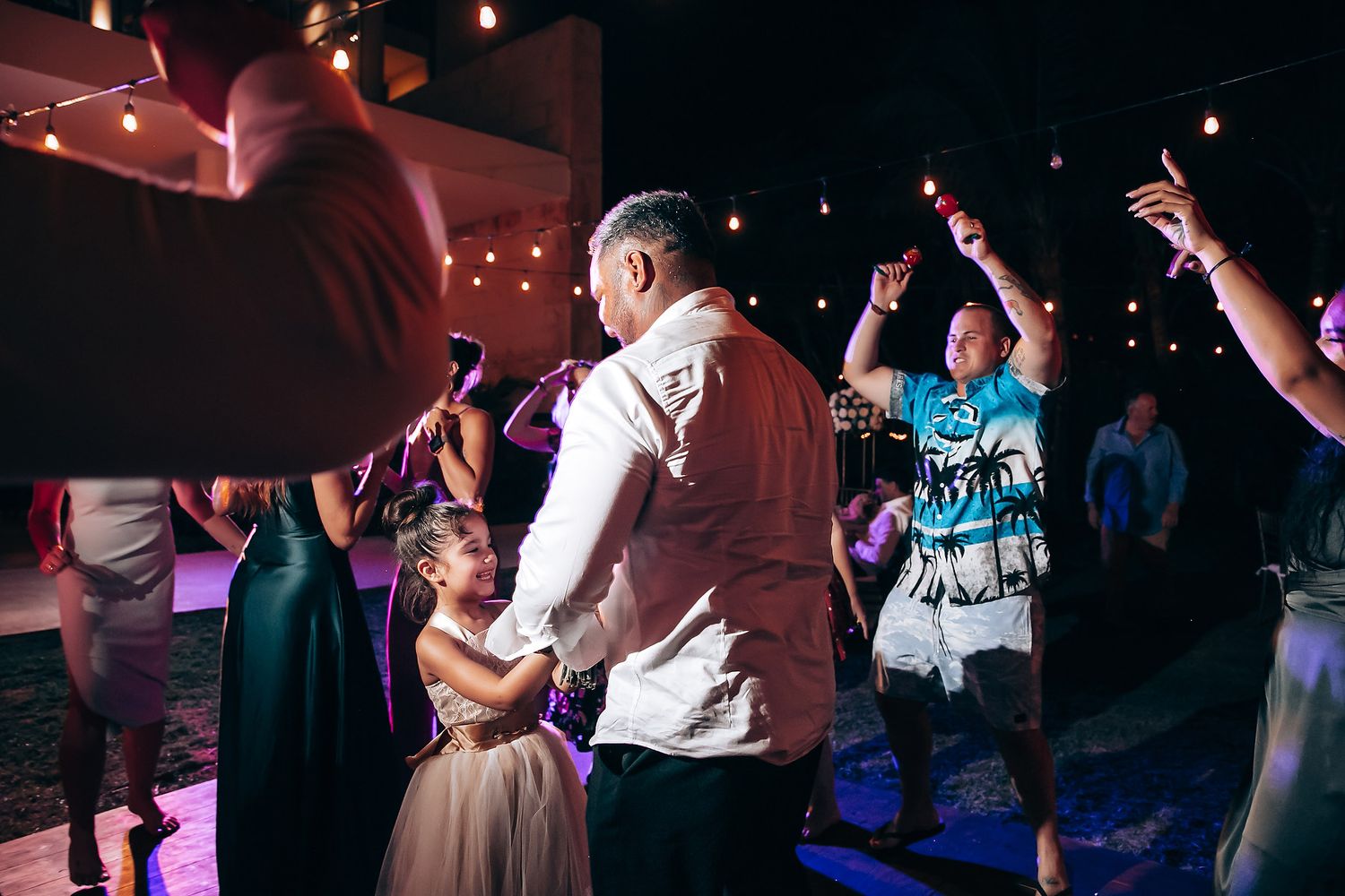 Wedding guests dancing and celebrating on a dimly lit dance floor.