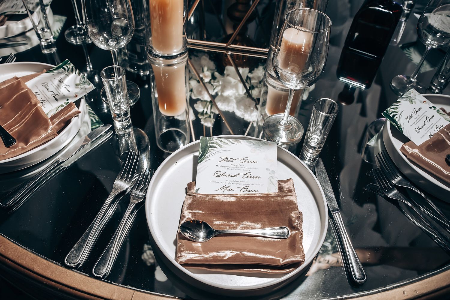 Wedding reception table settings with elegant glassware and metallic accents.