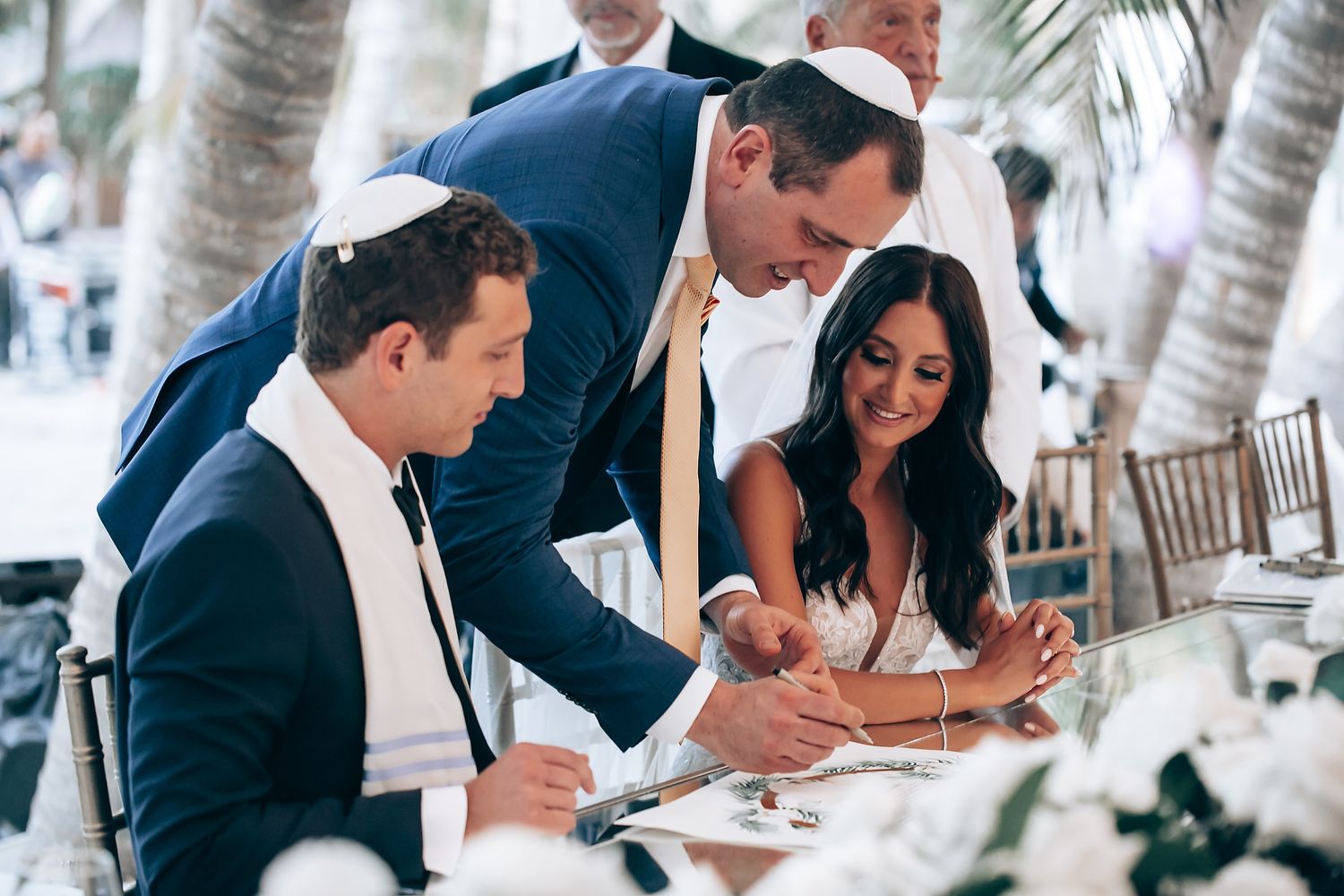 Wedding guests signing documents at an outdoor tropical venue.