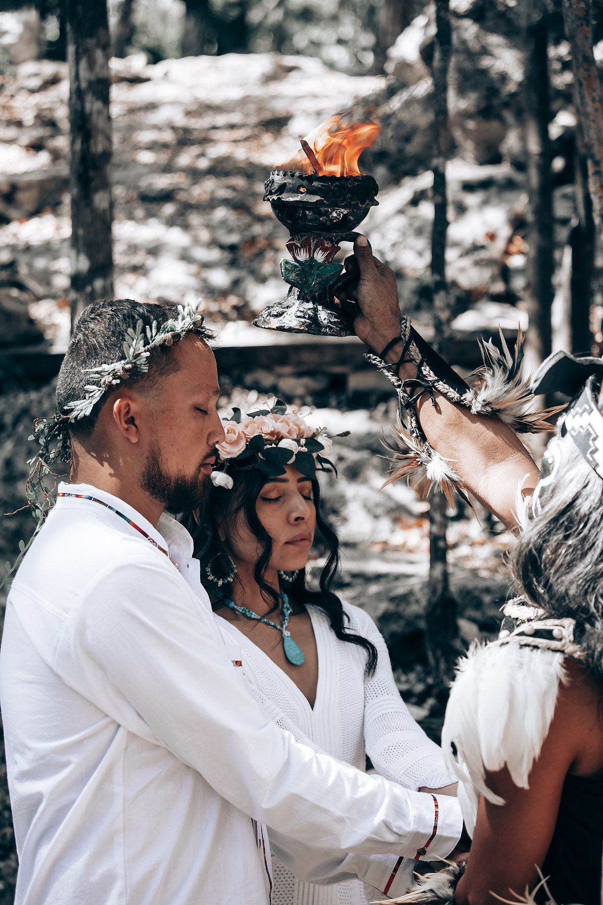 Group wearing ceremonial headdresses and white clothing performing traditional rituals outdoors.