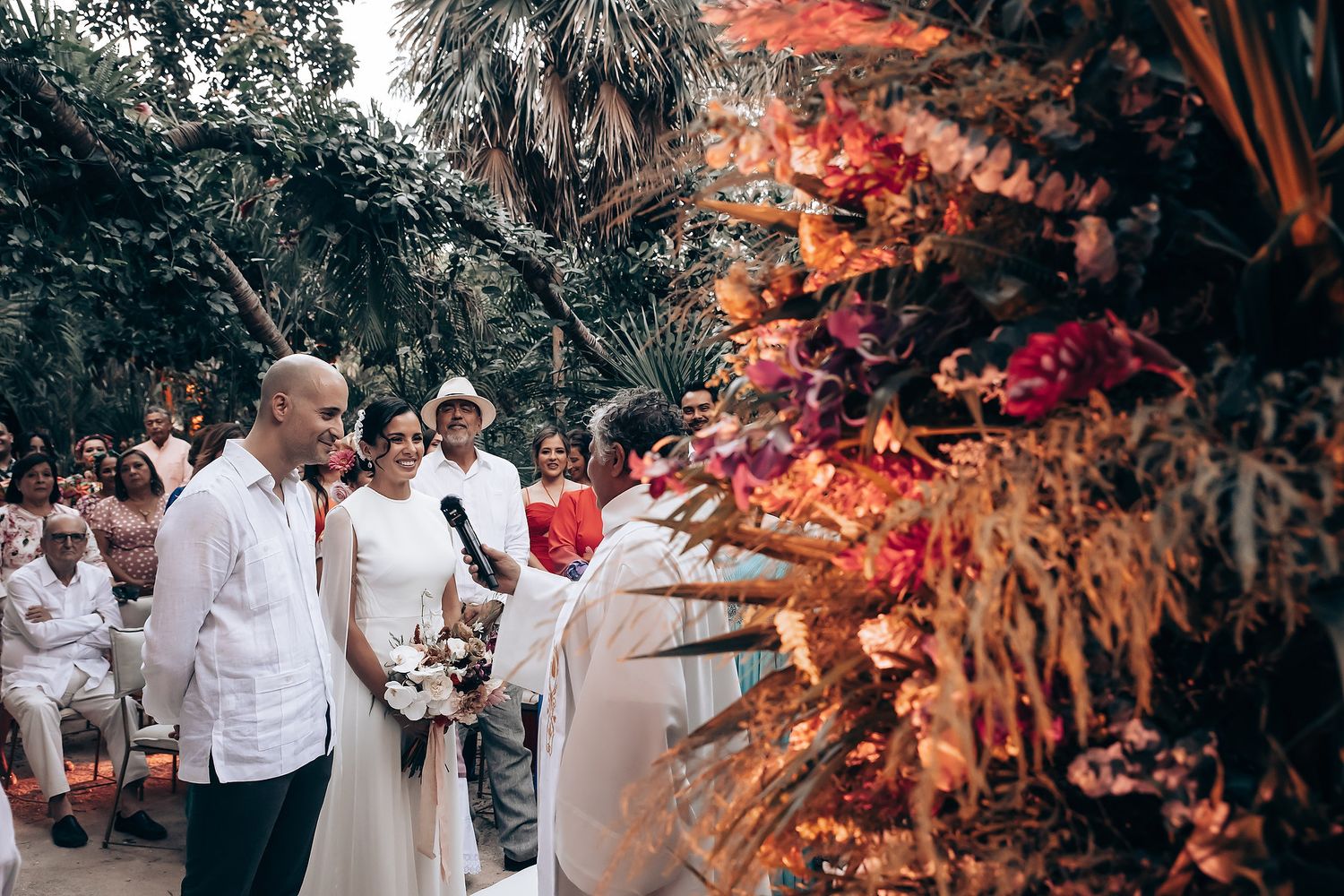 Guests gather at a tropical wedding reception with vibrant red floral decorations.