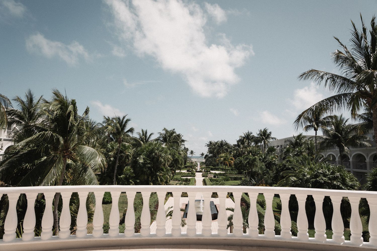 Elegant white balustrade terrace overlooking lush tropical palm trees and manicured grounds at a luxury resort wedding venue.