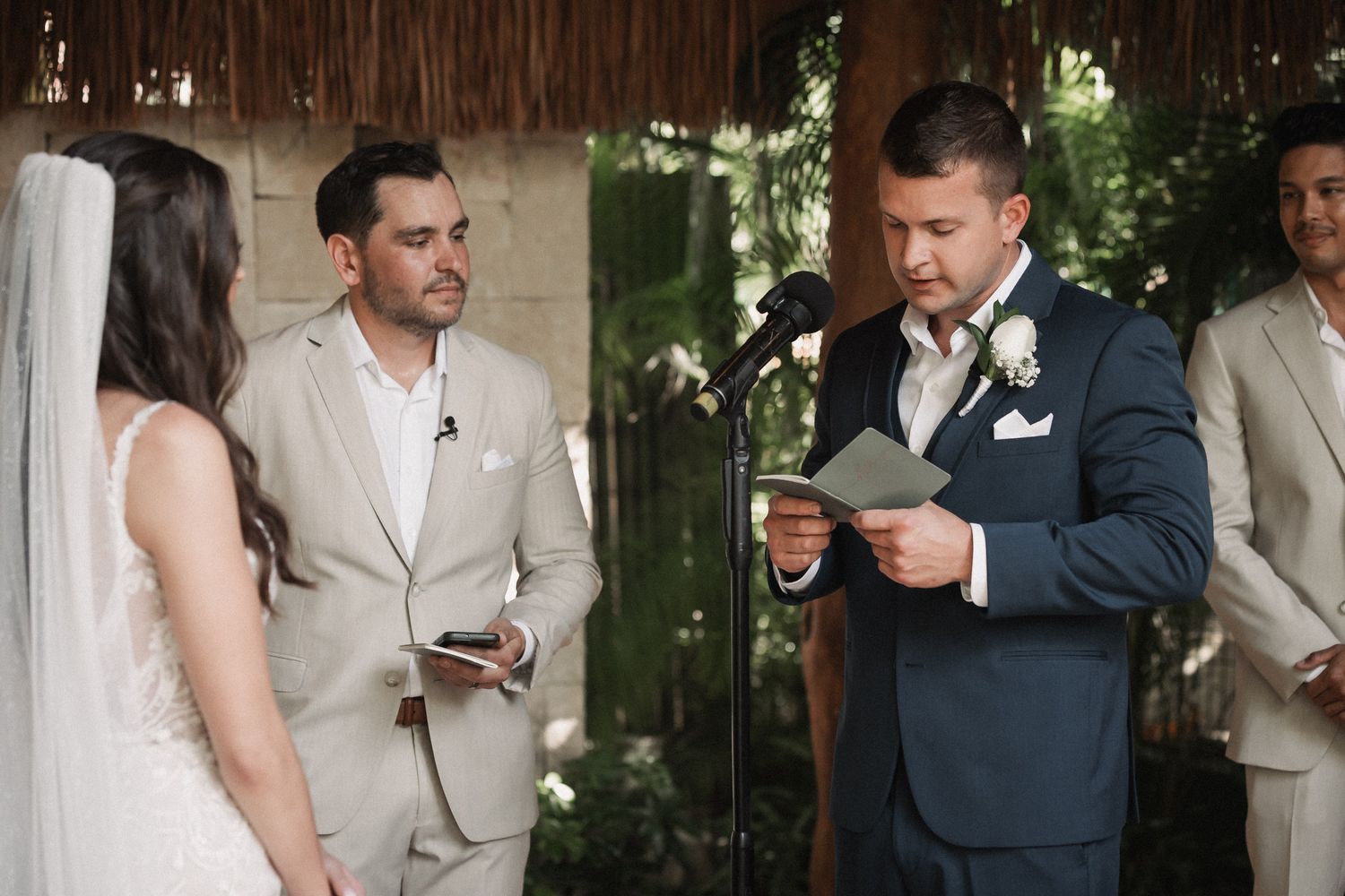 Groom reads heartfelt vows from a card during an intimate tropical wedding ceremony.