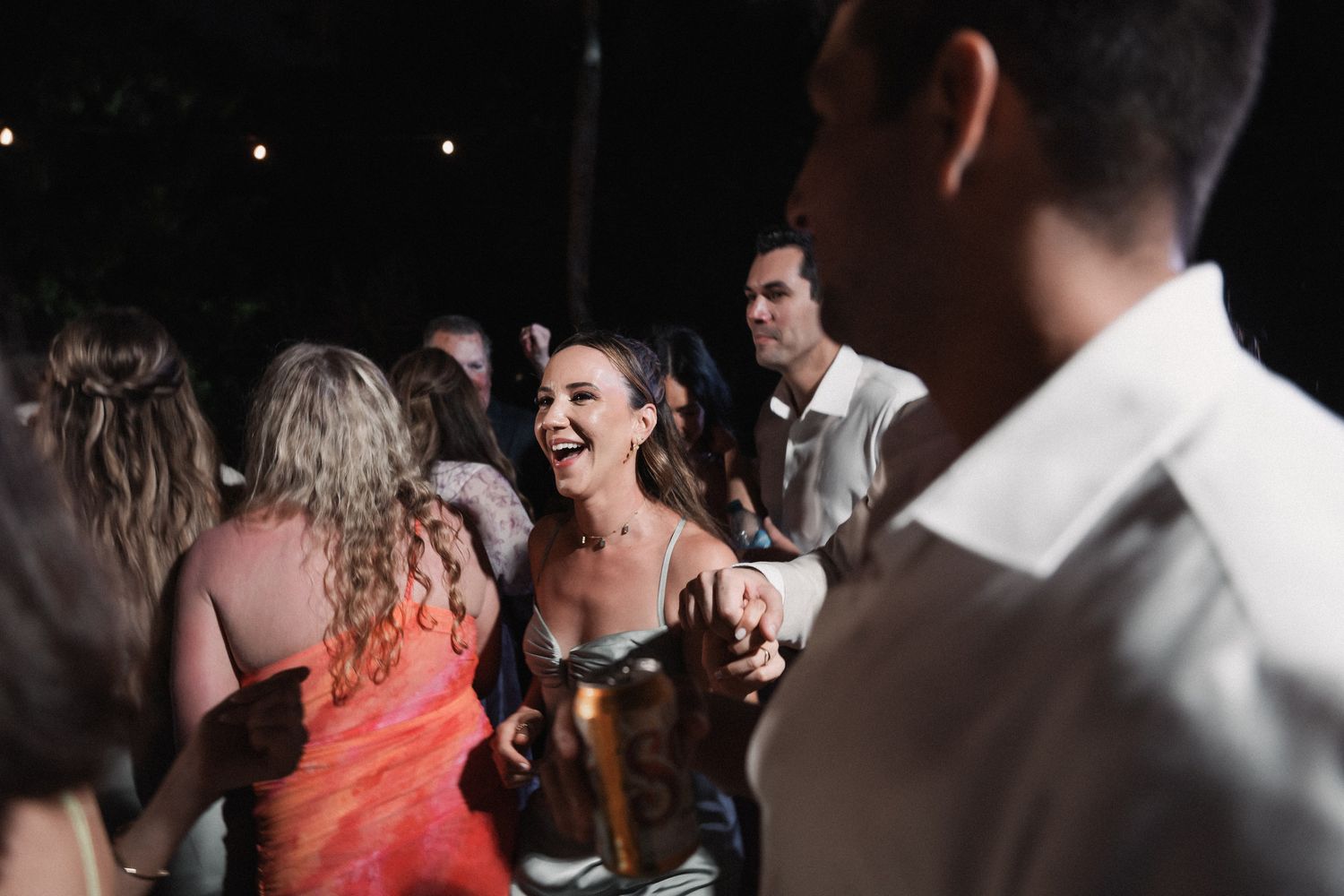 Joyful wedding guest in silver dress laughing and celebrating at outdoor evening wedding reception.