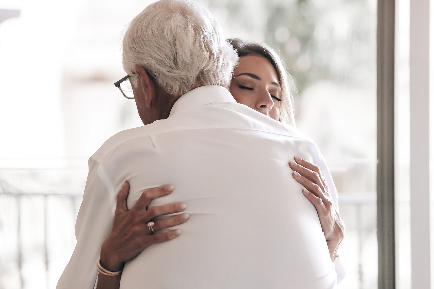 An elderly man and a younger woman embrace in a warm hug.