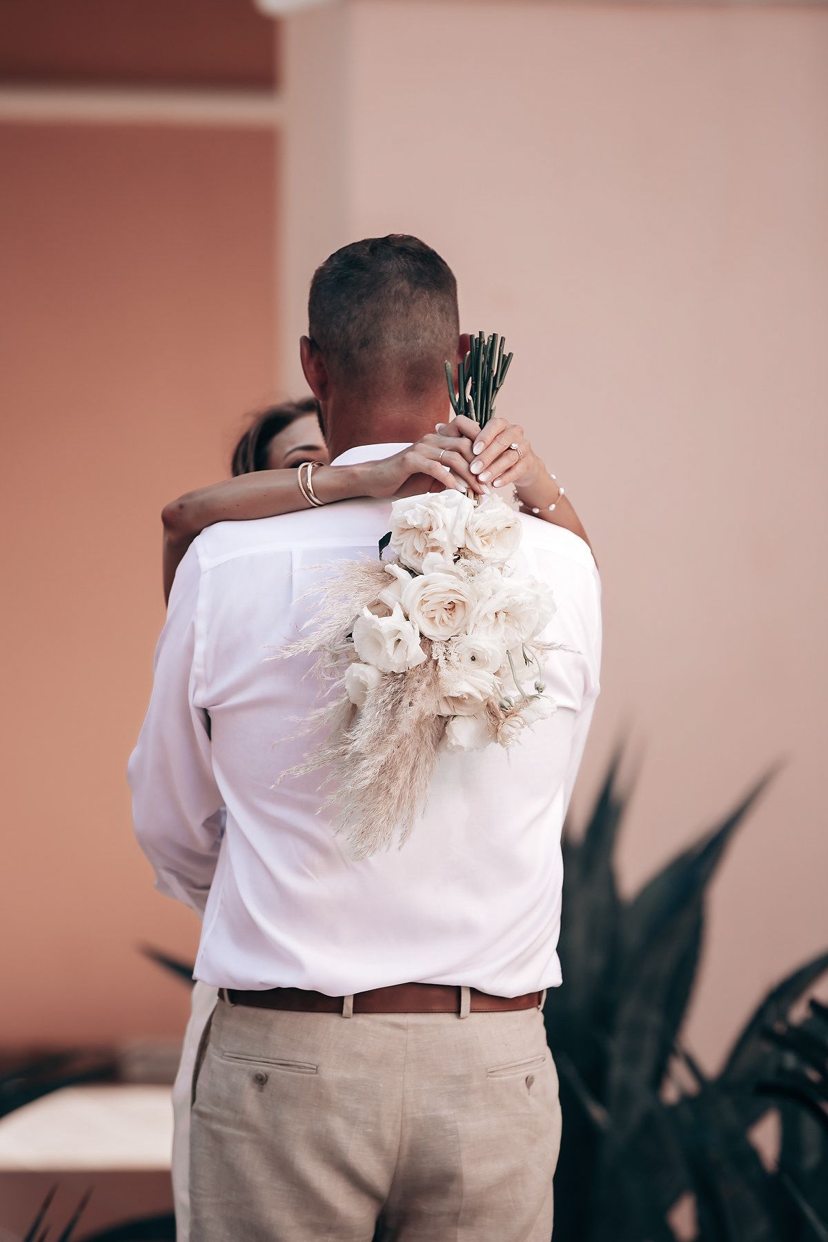 A man embraces a woman in a white dress at a wedding ceremony.